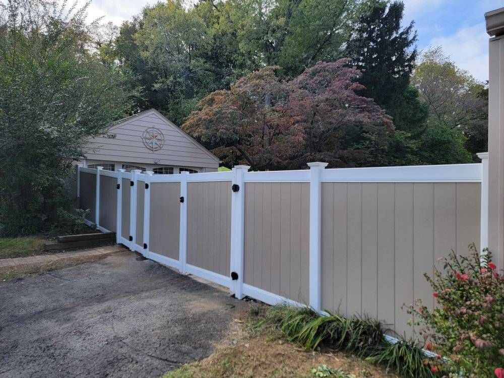 Tan and white vinyl fence with a gate, in front of greenery.