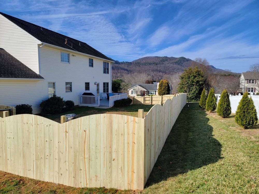 Wooden fence surrounding a backyard with a two-story house, evergreens, and mountains in the background.
