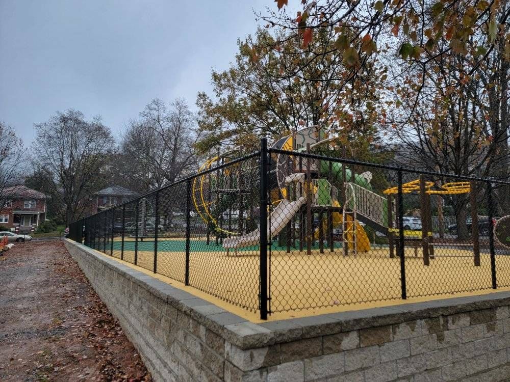 Playground with black fence, yellow play surface, and climbing structures on a cloudy day.