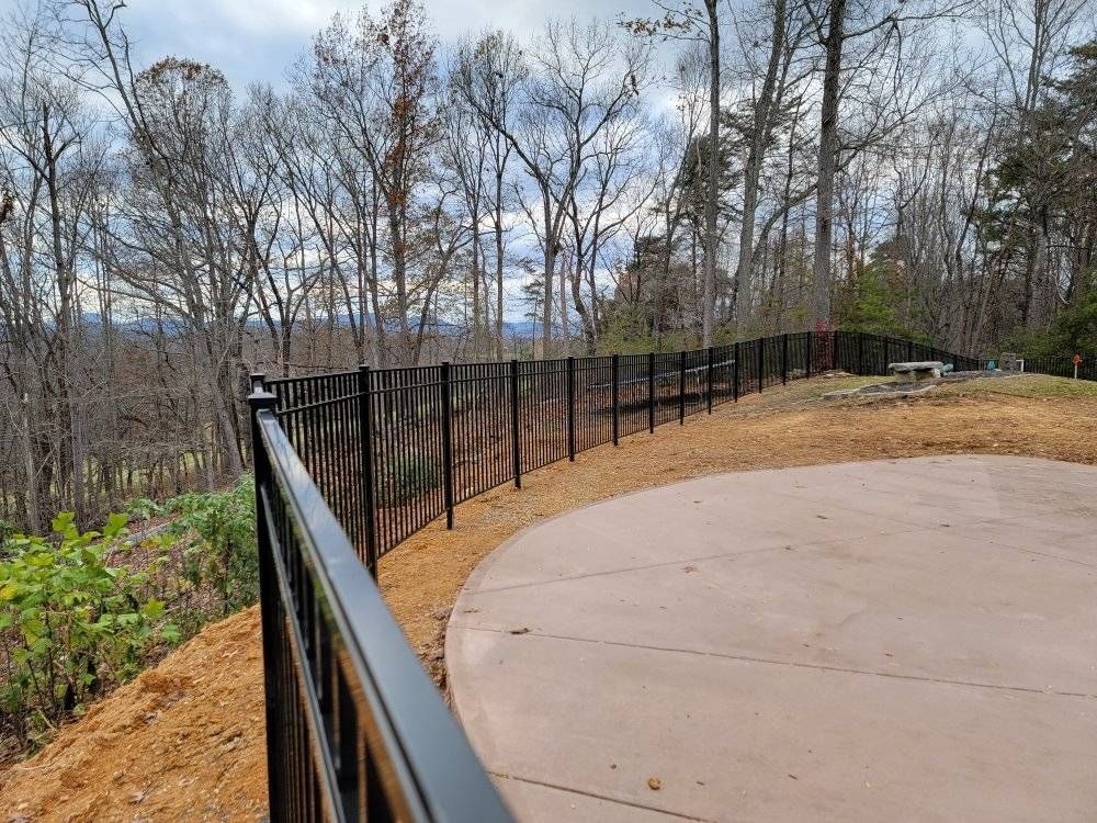 Black metal fence along a concrete patio on a hillside, overlooking trees.
