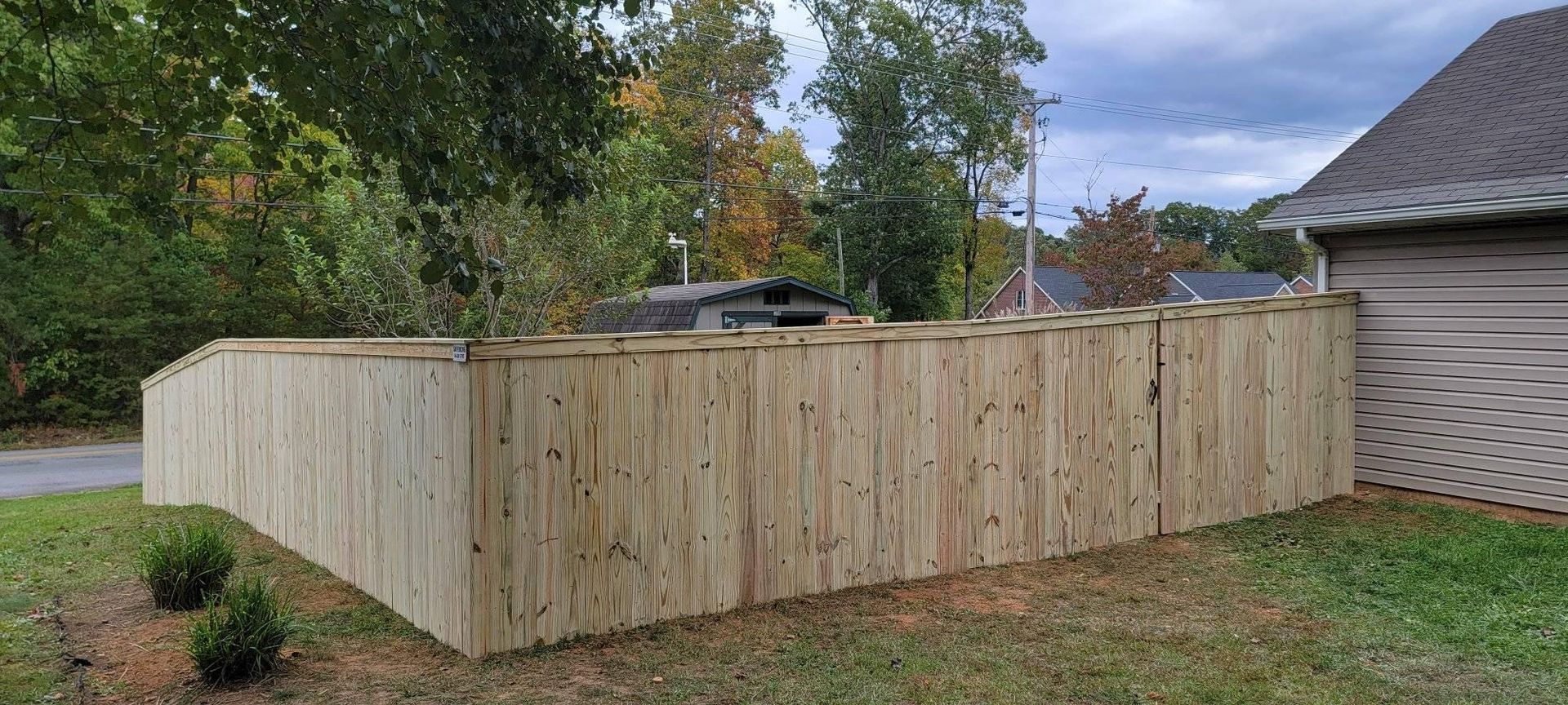 Wooden fence in front of a house, with grass and trees in the background. Overcast day.