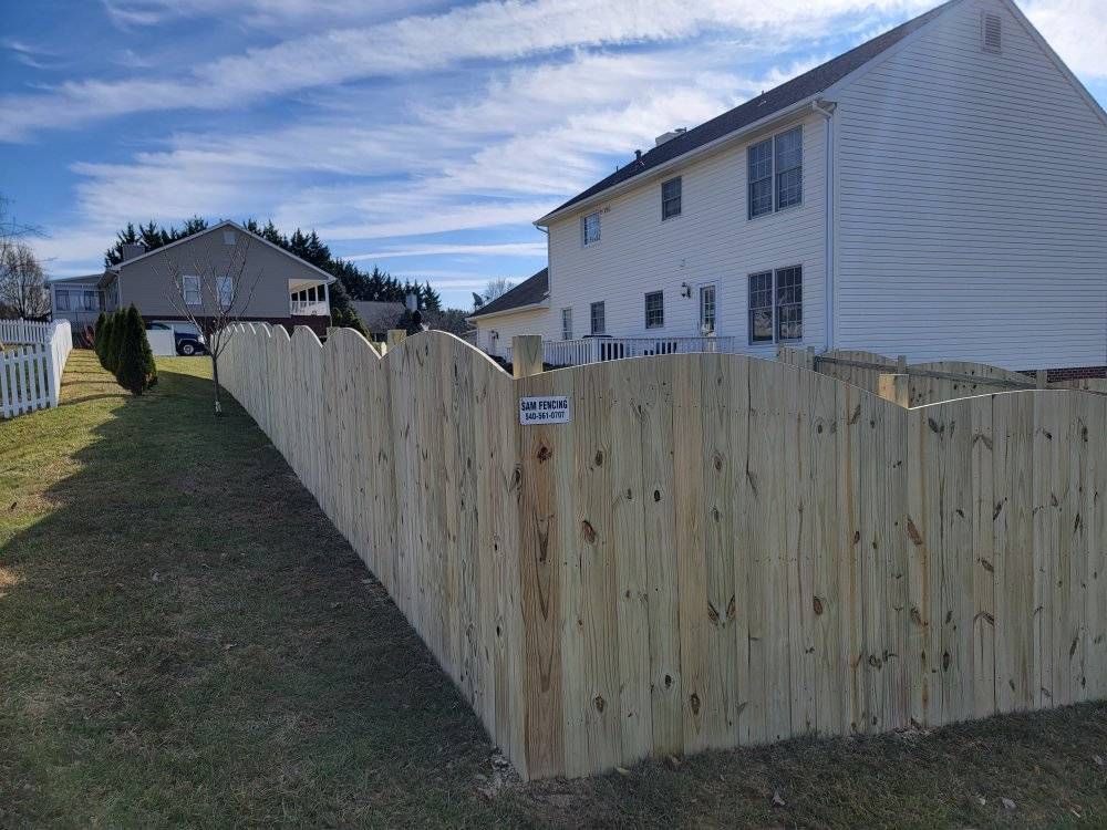 Wooden fence along a grassy yard, beside a two-story house under a blue sky.