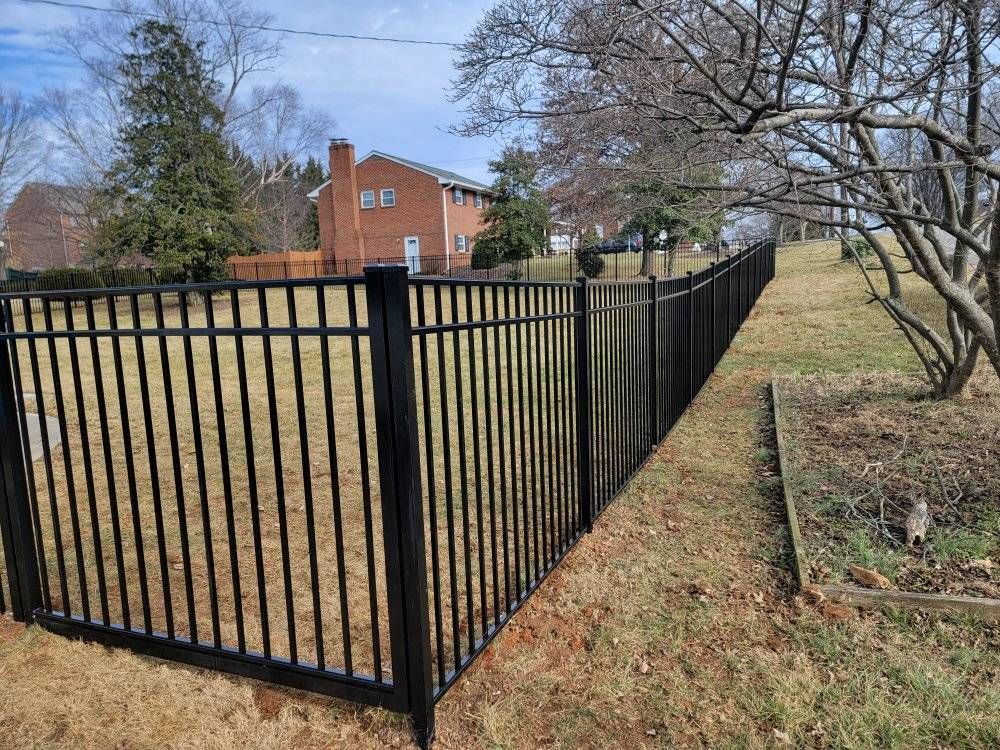 Black metal fence along a grassy yard, with a brick house and trees in the background.