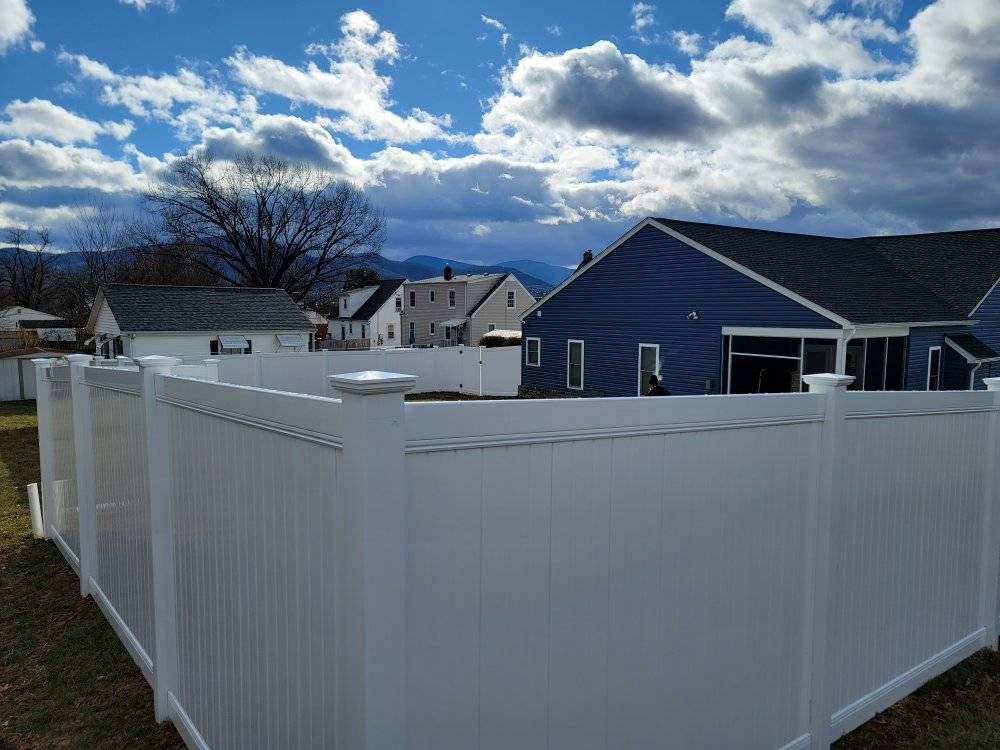 White vinyl fence surrounding a backyard with blue house and cloudy sky.