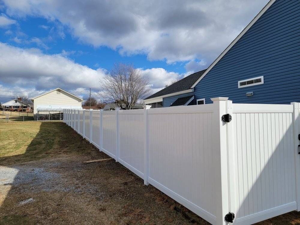 White vinyl fence running along a green lawn beside a blue house under a partly cloudy sky.