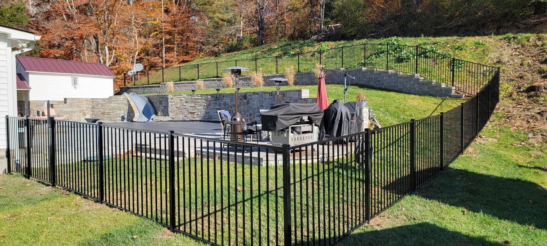Black fence encloses a backyard with a pool, patio furniture, and a hillside in the background.