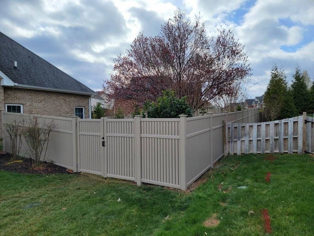 Tan vinyl fence enclosing a backyard with a gate, trees, and cloudy sky.