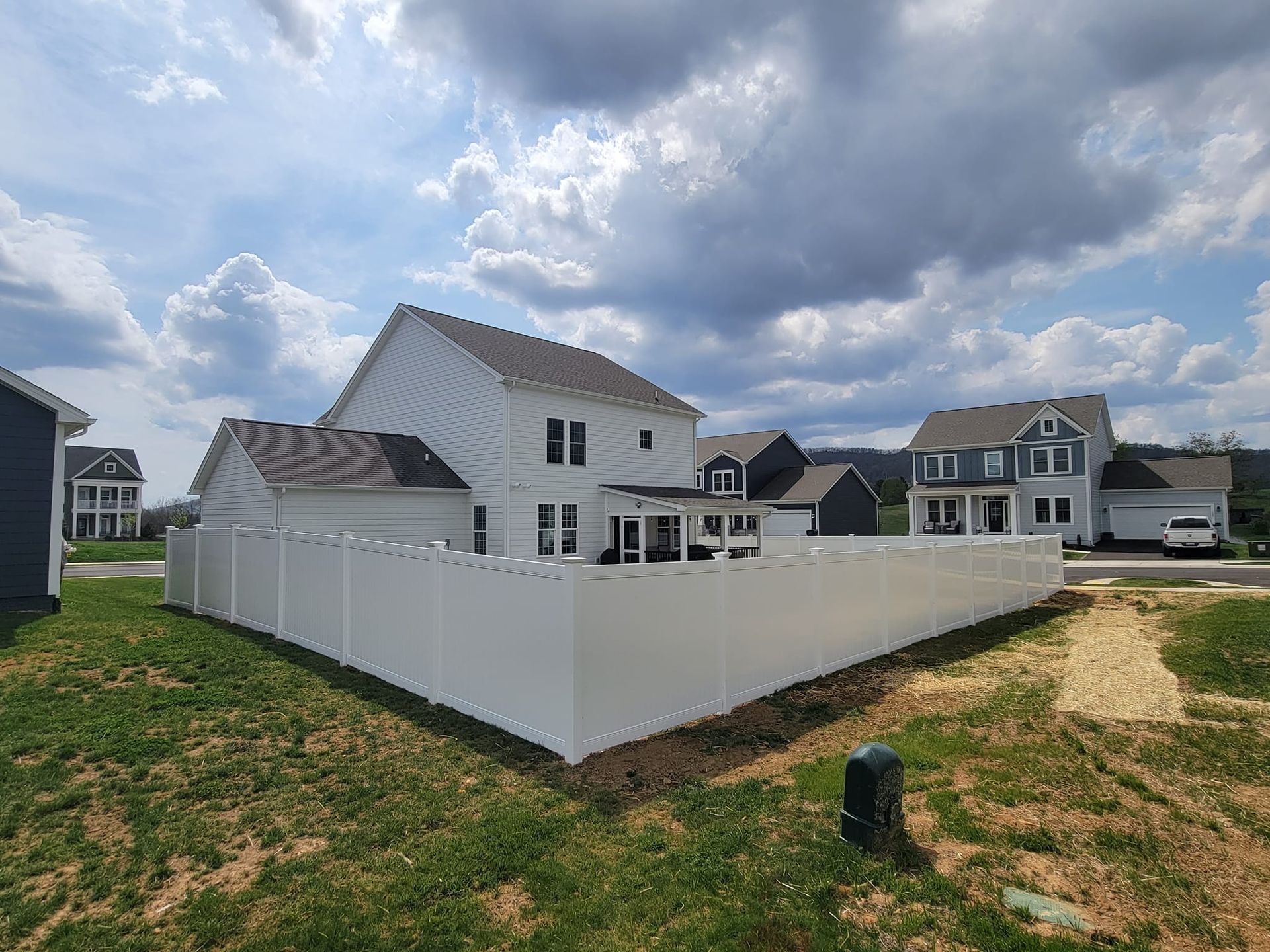 White vinyl fence surrounding a two-story house with white siding and dark roof, cloudy sky.
