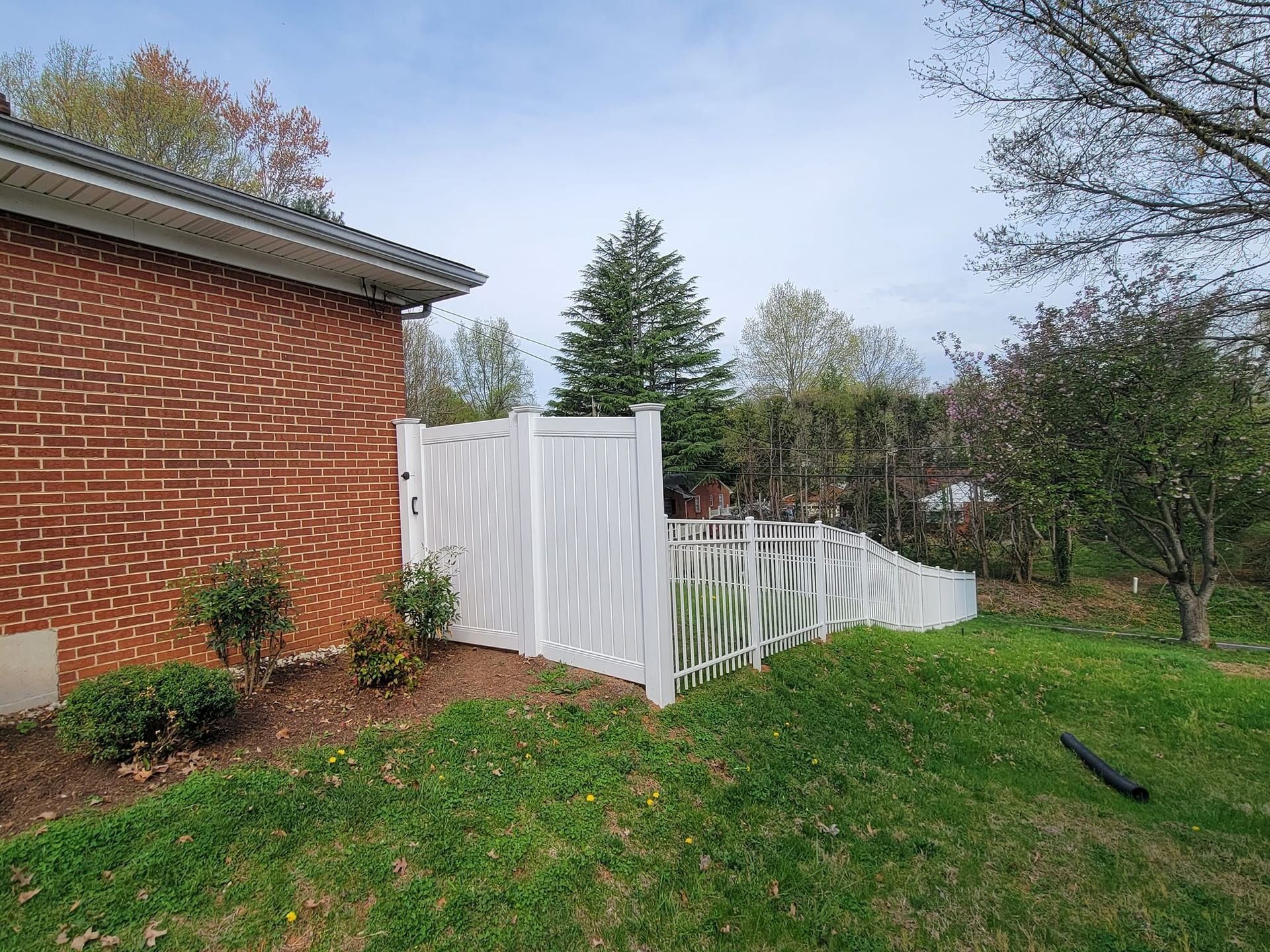 White decorative fence next to a brick building. Green grass and trees in the background.