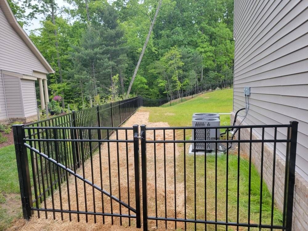 Black metal fence surrounding a yard with an air conditioning unit and gate near a house.