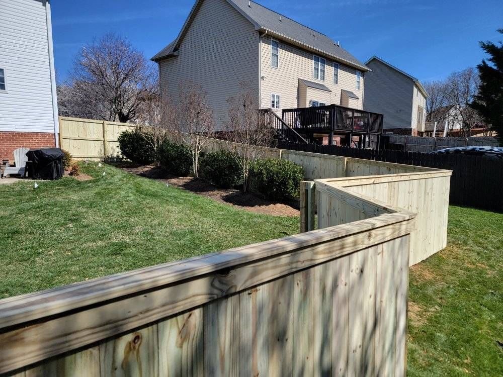 Wooden fence in a backyard with grass, shrubs, and houses.