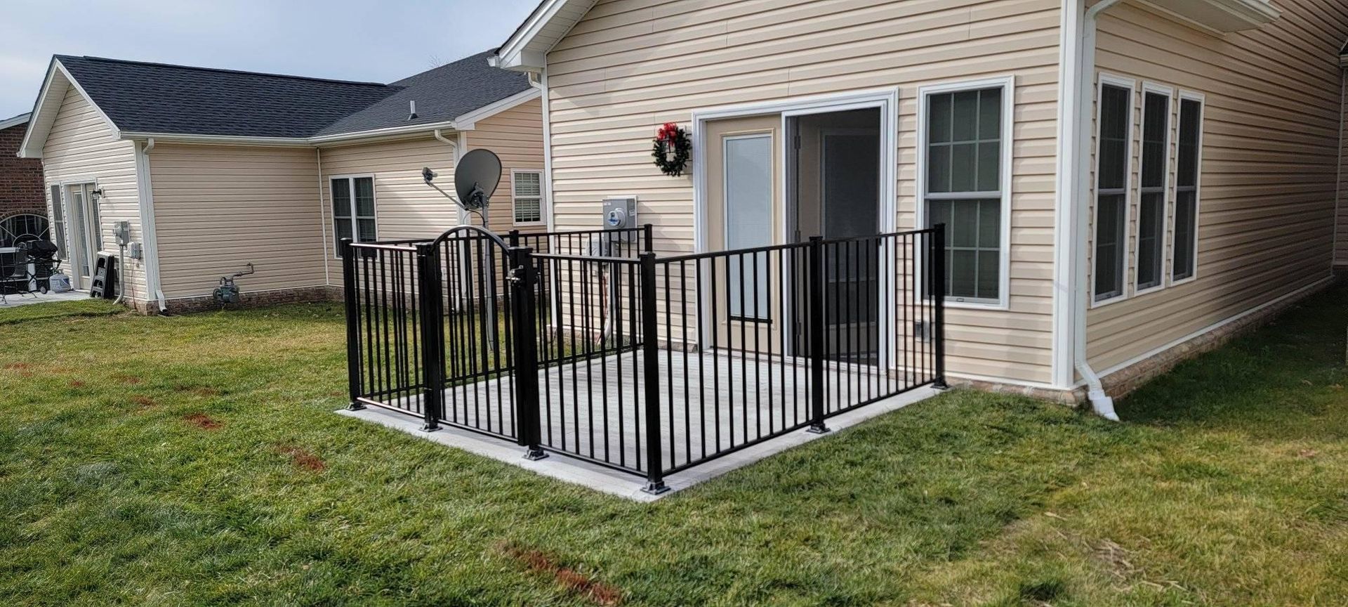 Black fence encloses a patio outside a beige house. Grass surrounds the patio.