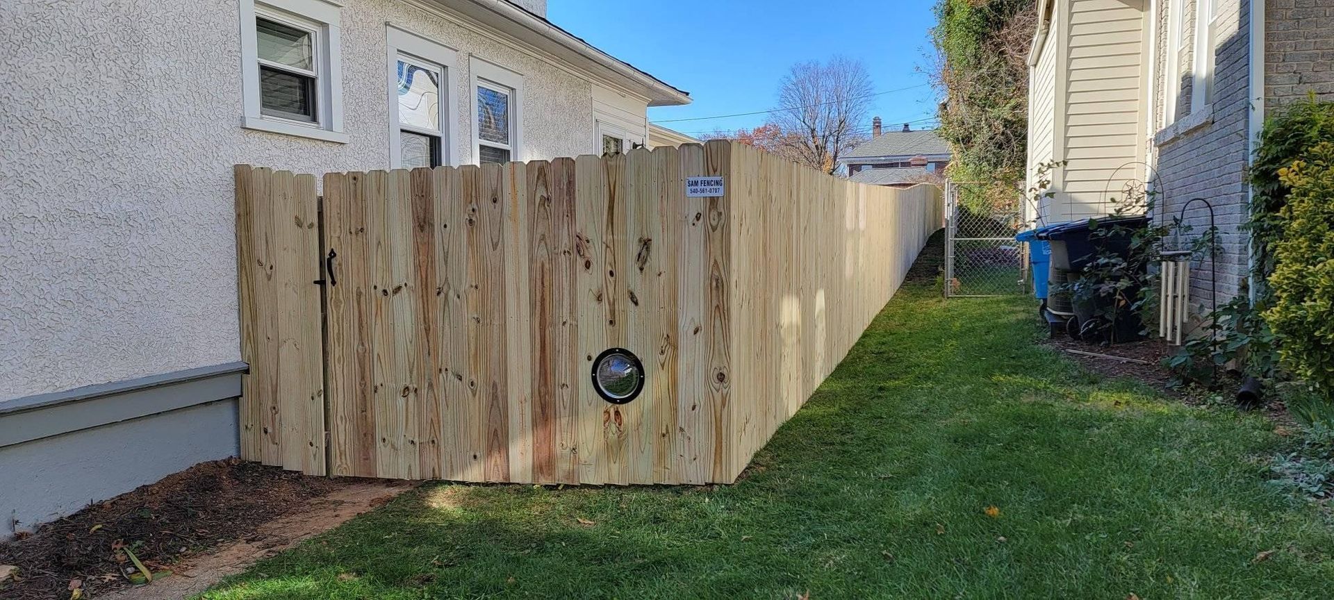 Wooden fence separating two houses; a round pipe visible within.
