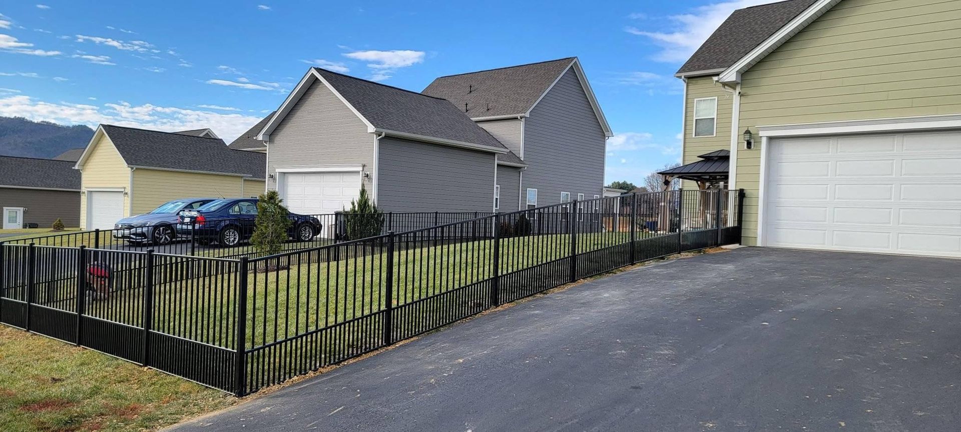 Houses with a black fence, cars in driveway, clear sky.