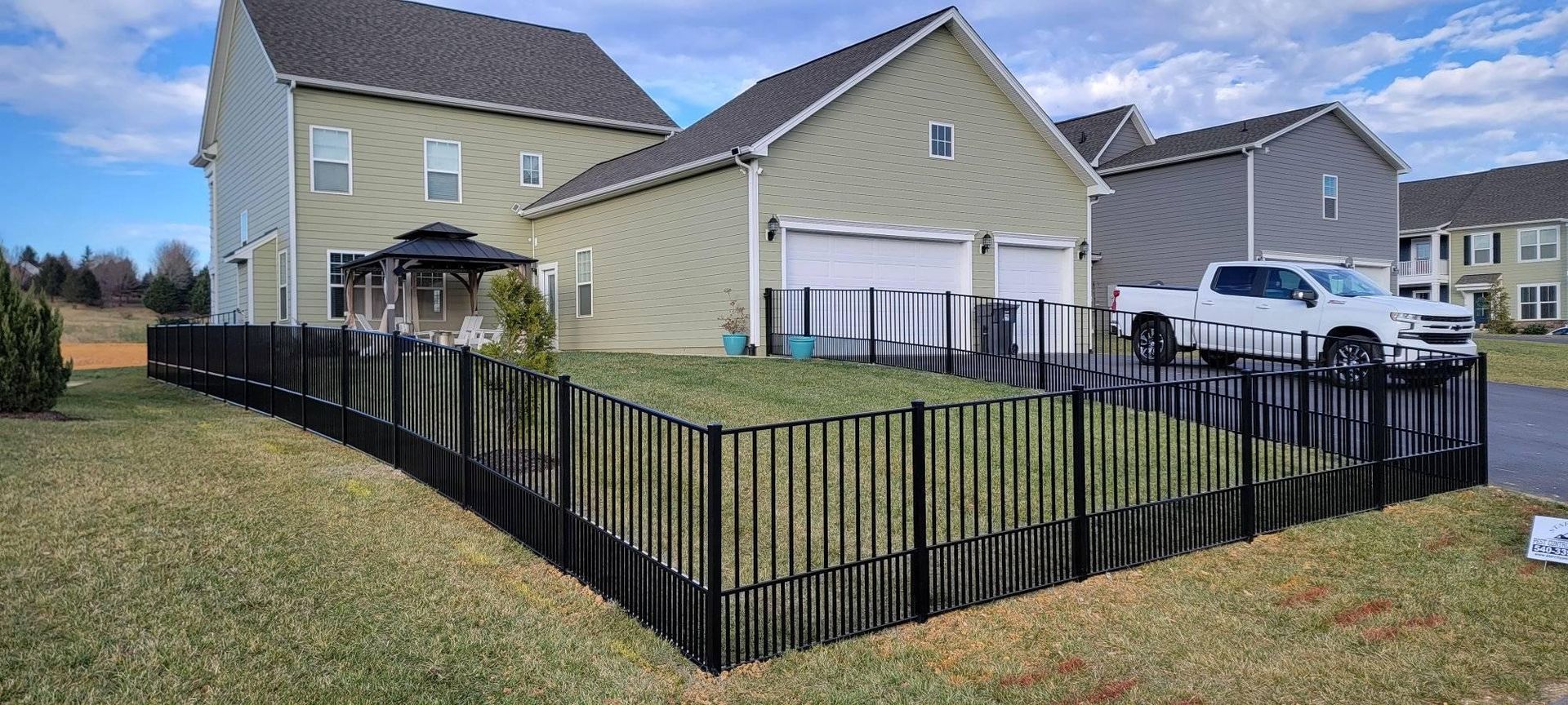 Black fence around a grassy backyard with a house, garage, and white truck parked inside.