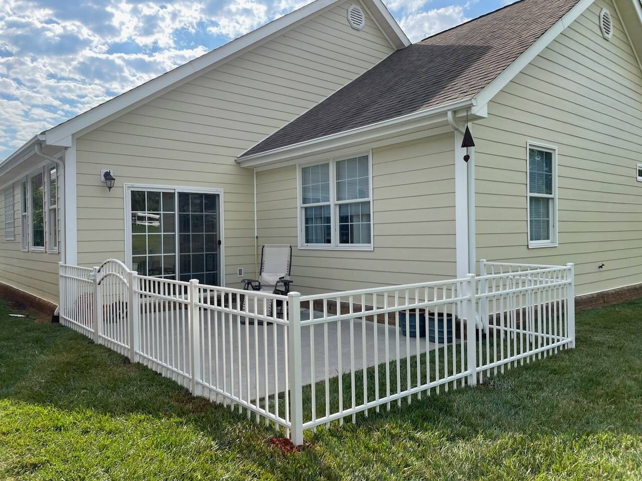 Tan house with white railing surrounding a patio on green grass.
