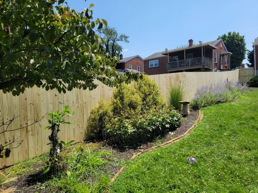 Wooden fence along a yard with landscaping and houses in the background on a sunny day.