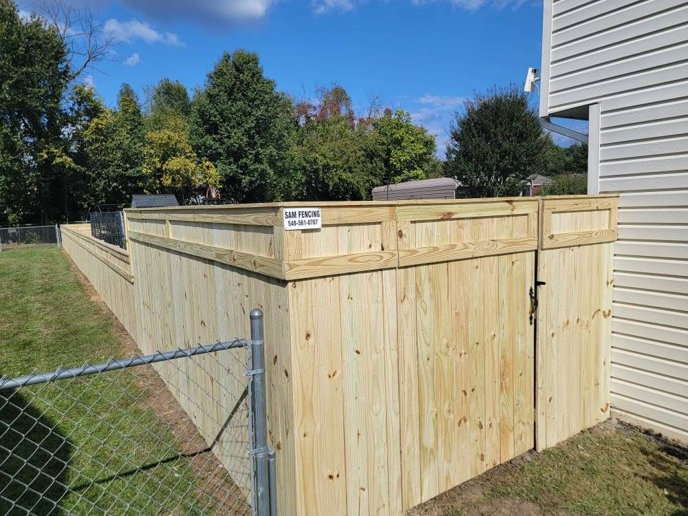 Wooden privacy fence along a green lawn, adjacent to a house with white siding, under a blue sky.