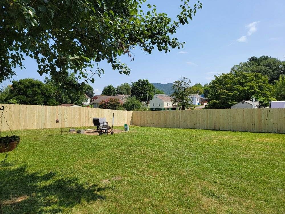 A sunny backyard enclosed by a wooden fence, with a grill and trees in the background.