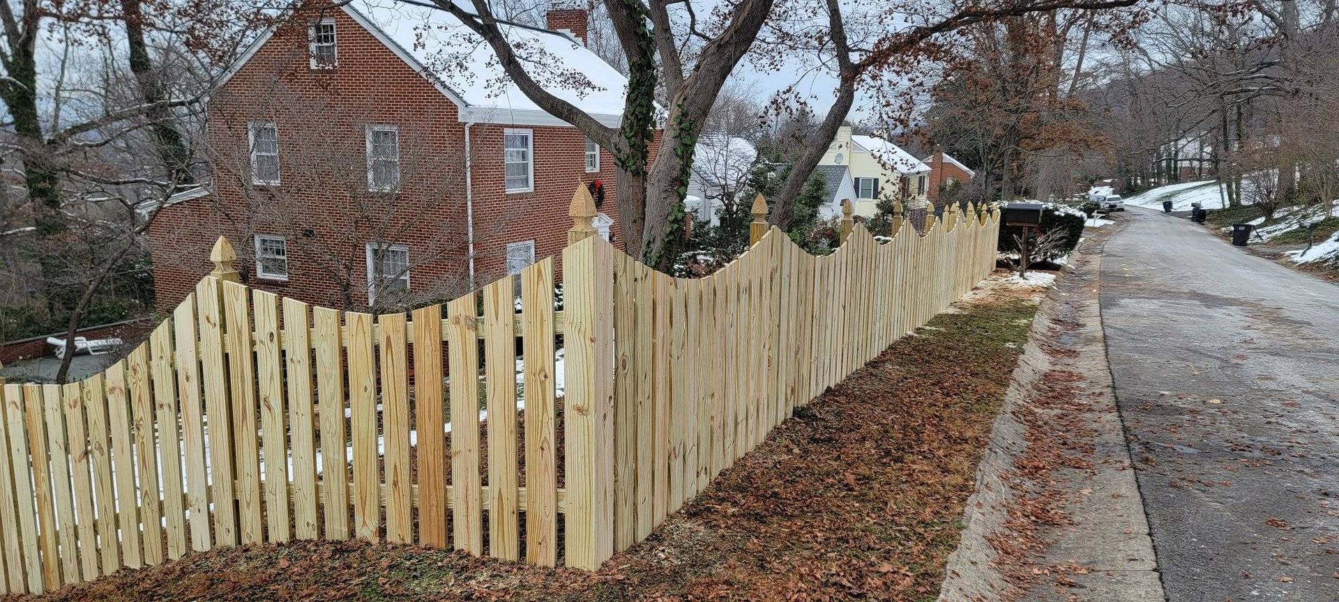 Wooden picket fence along a street lined with houses; overcast day.