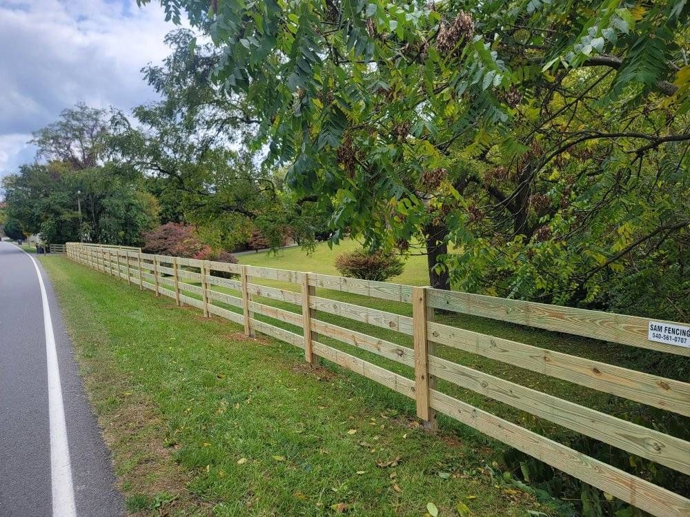 Wooden fence along a road next to green grass and trees.