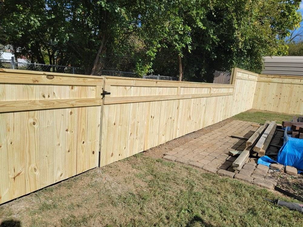 Wooden fence in backyard, with gate and retaining wall.