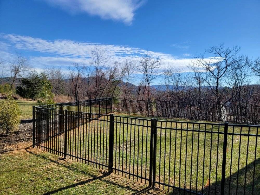 Black metal fence in a yard with a mountain backdrop under a blue sky with scattered clouds.