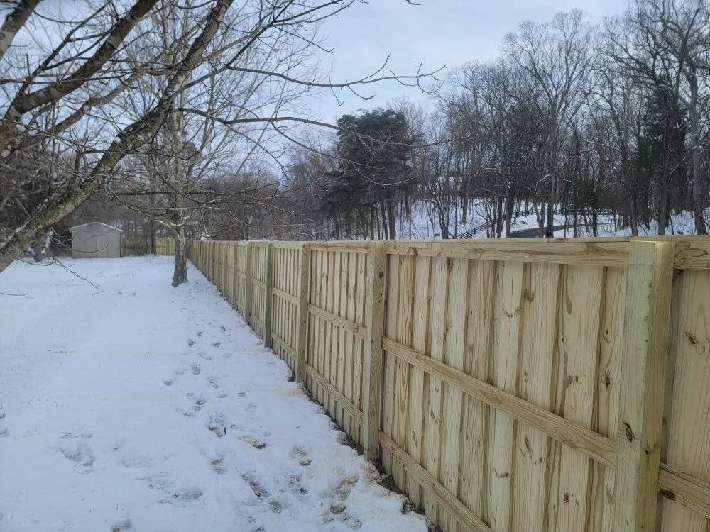 Wooden fence in a snowy, outdoor setting with bare trees in the background.