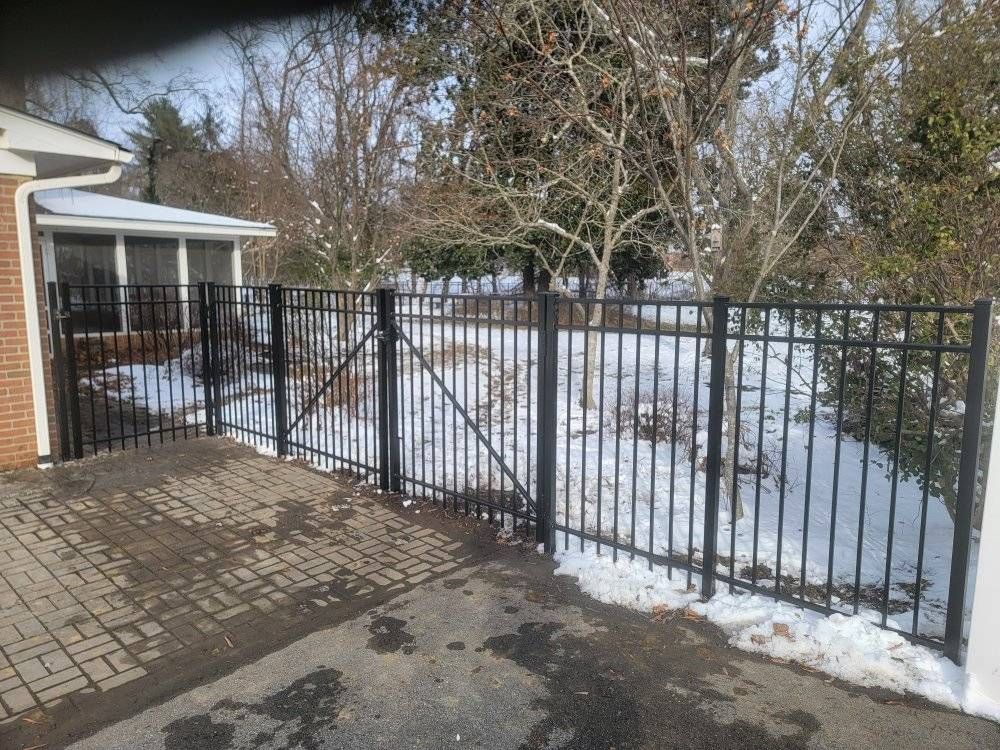 Black metal fence with gate in front of a snow-covered yard, next to a brick building.
