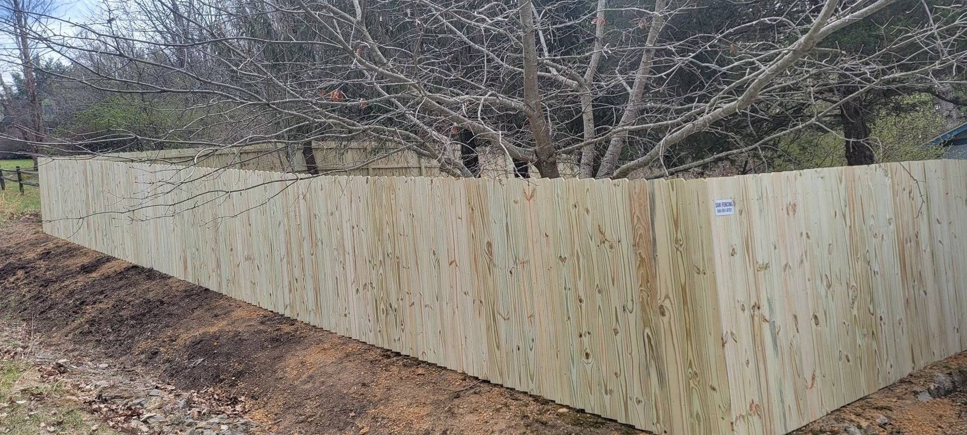 A long, wooden barrier surrounds a tree, set in a dirt area.
