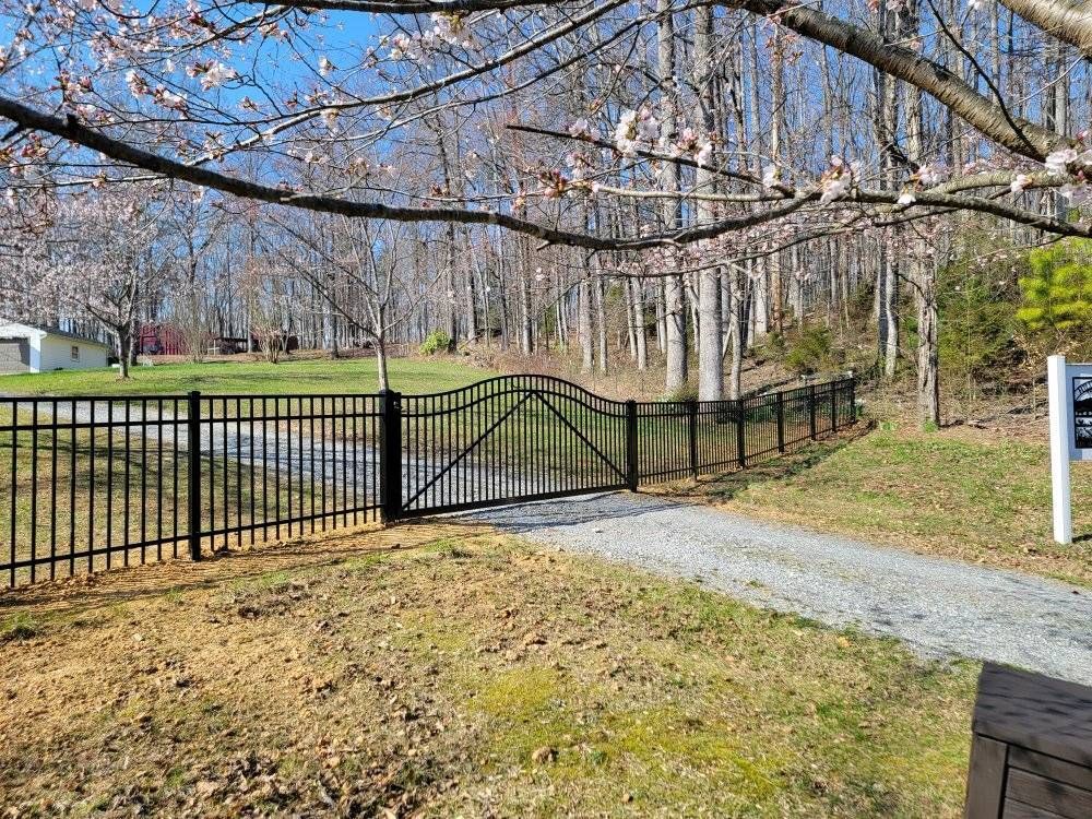 Black metal fence with gate and gravel driveway leading into woods.