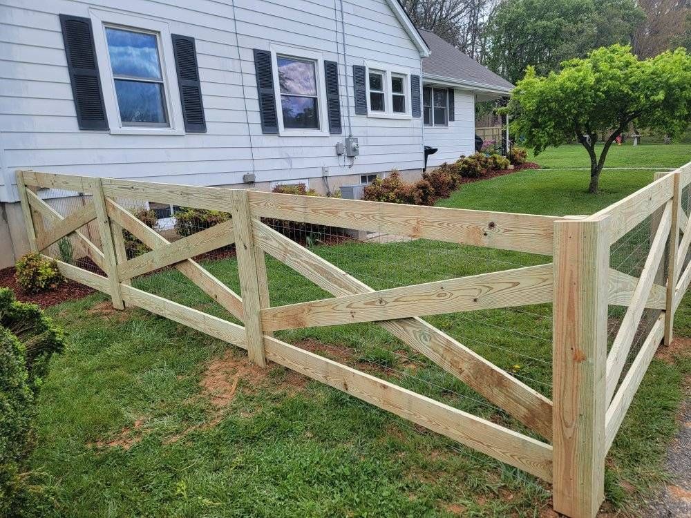 Wooden fence with crisscross design borders a house with white siding and black shutters.
