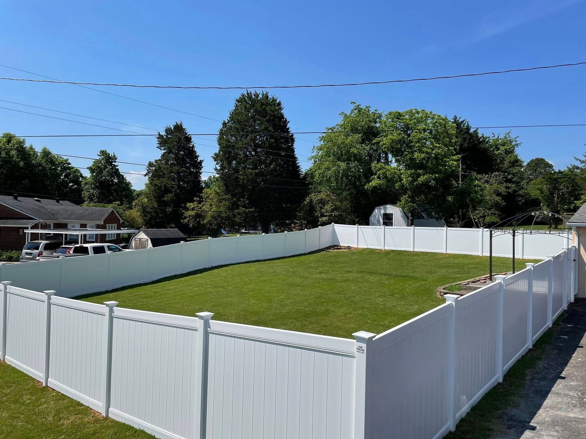 A rectangular backyard with white fence and green lawn under a bright blue sky.