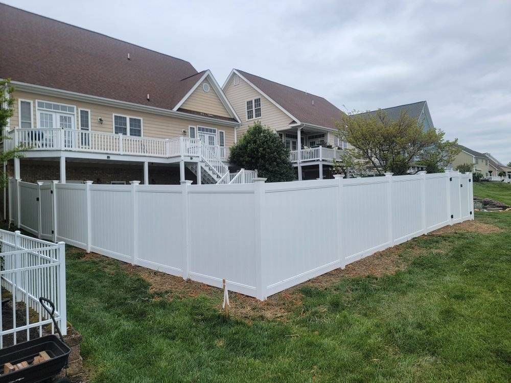 White vinyl fence surrounds a backyard with a two-story beige house and deck; cloudy sky.