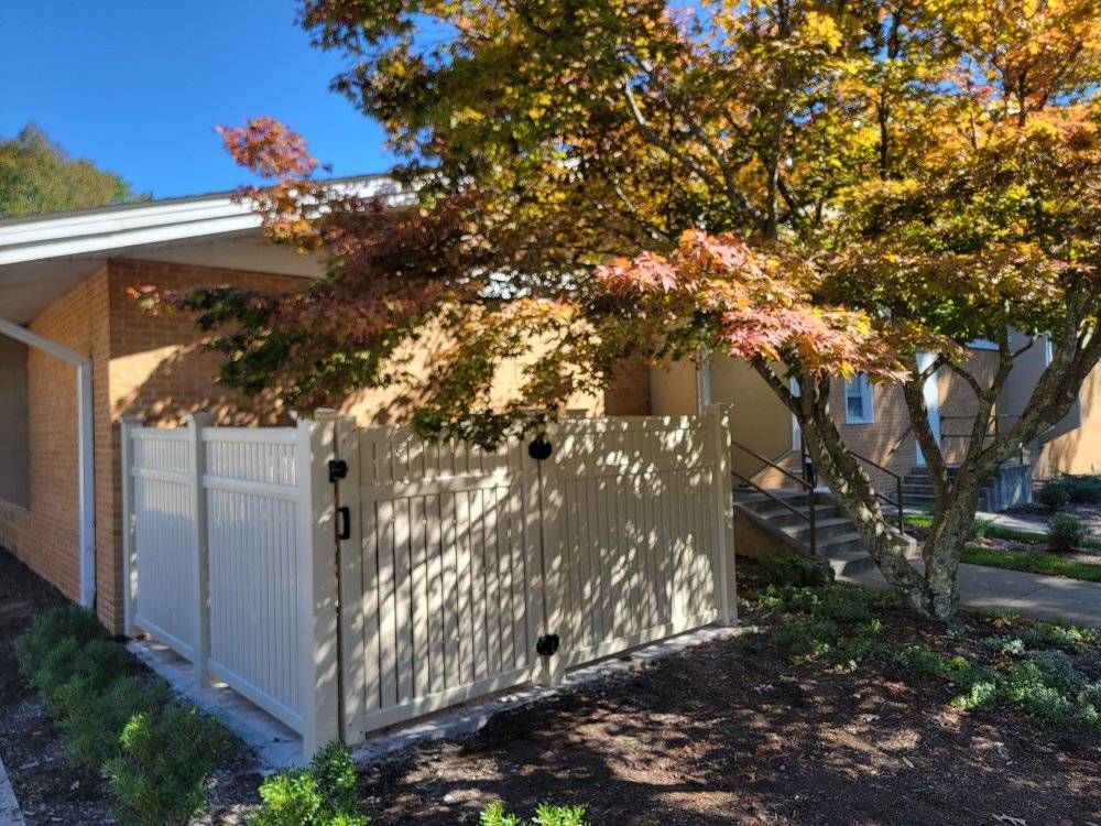 Beige fence in front of a building with a tree in fall foliage.