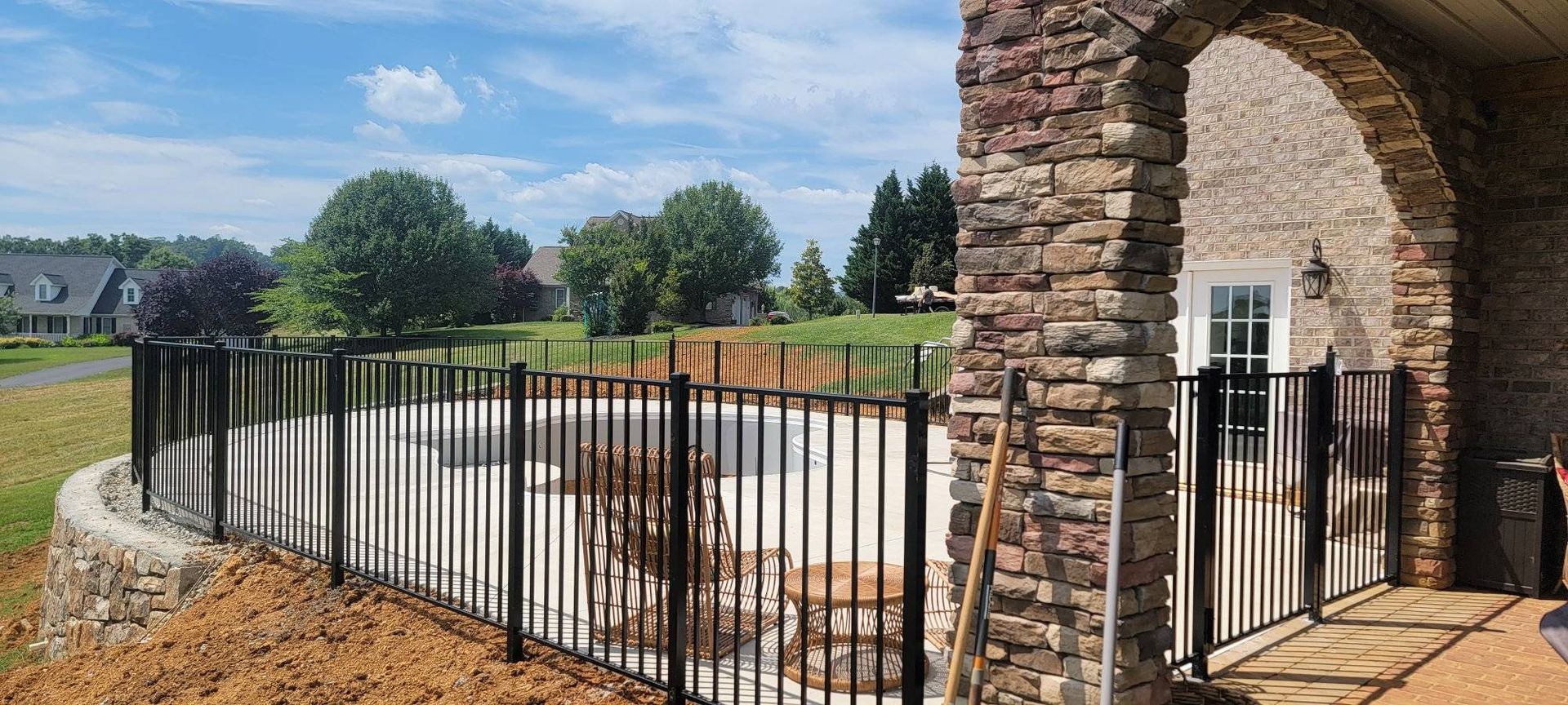 A black metal fence surrounds a pool with trees in the background, a stone archway on the right.
