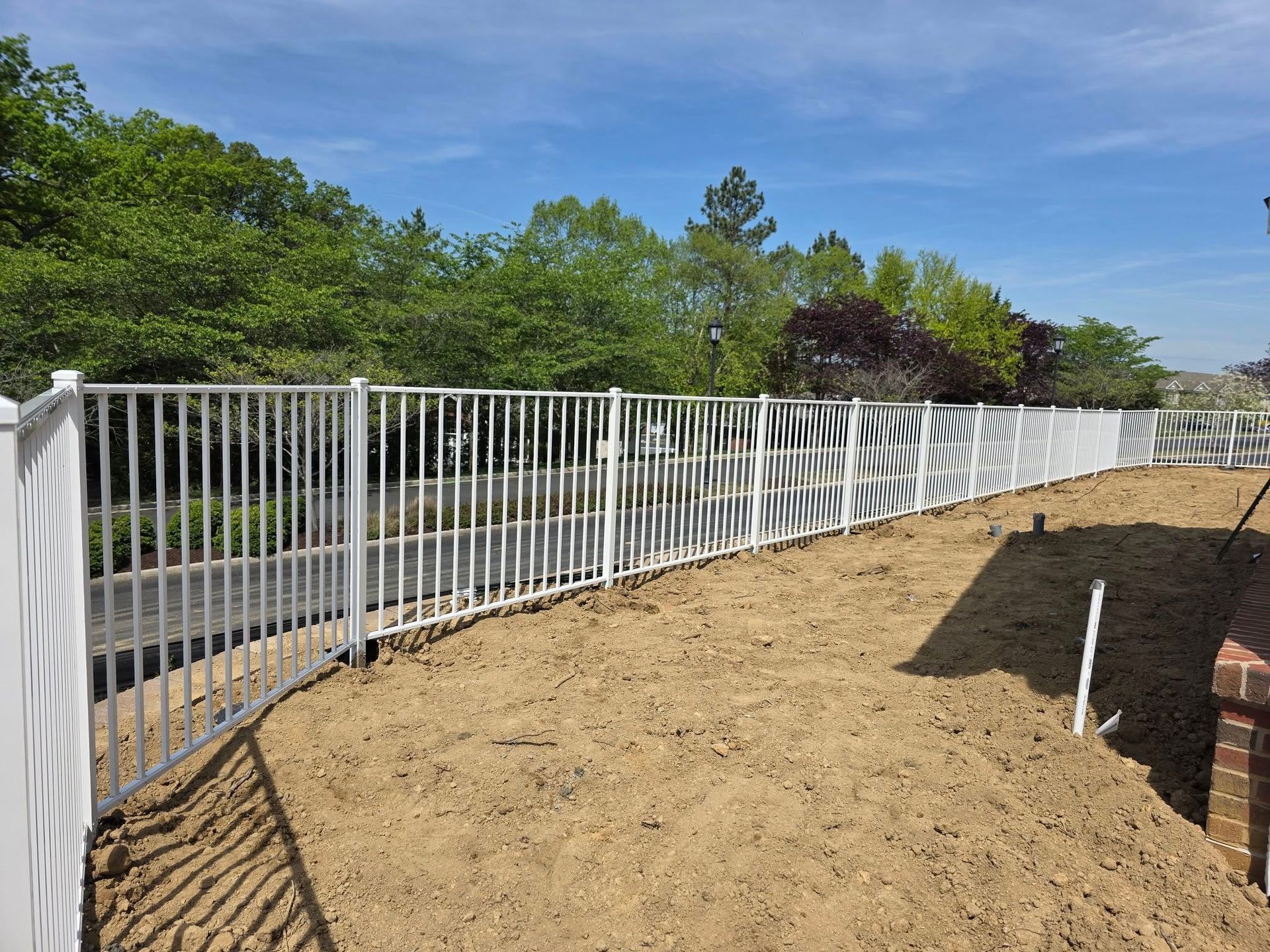 White metal fence in yard, with gate open. Striped privacy screen attached to the fence. Sunny day.