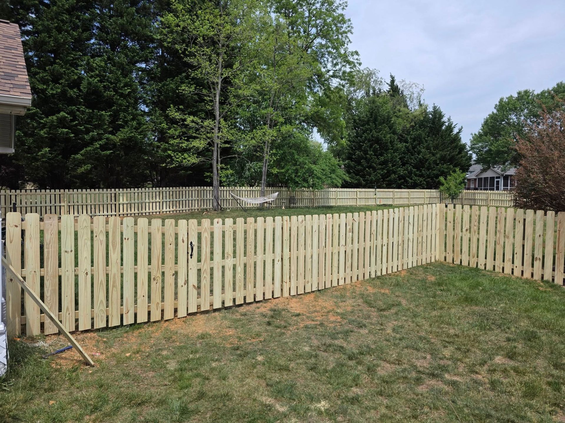 Wooden picket fence surrounding a grassy backyard with trees in the background.