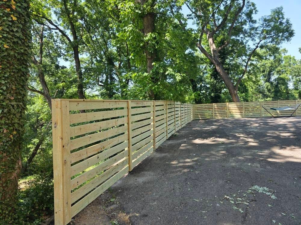 Wooden horizontal slat fence in a yard with trees.