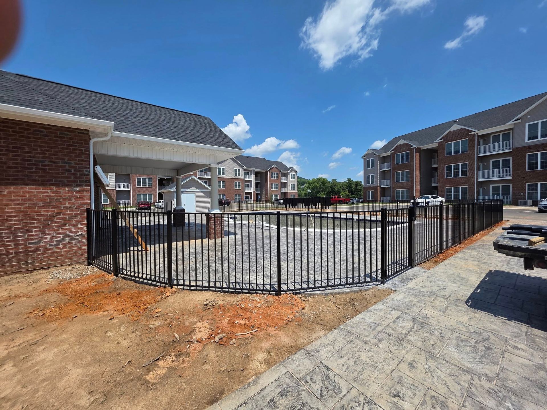 A fenced-in swimming pool in front of apartment buildings on a sunny day.