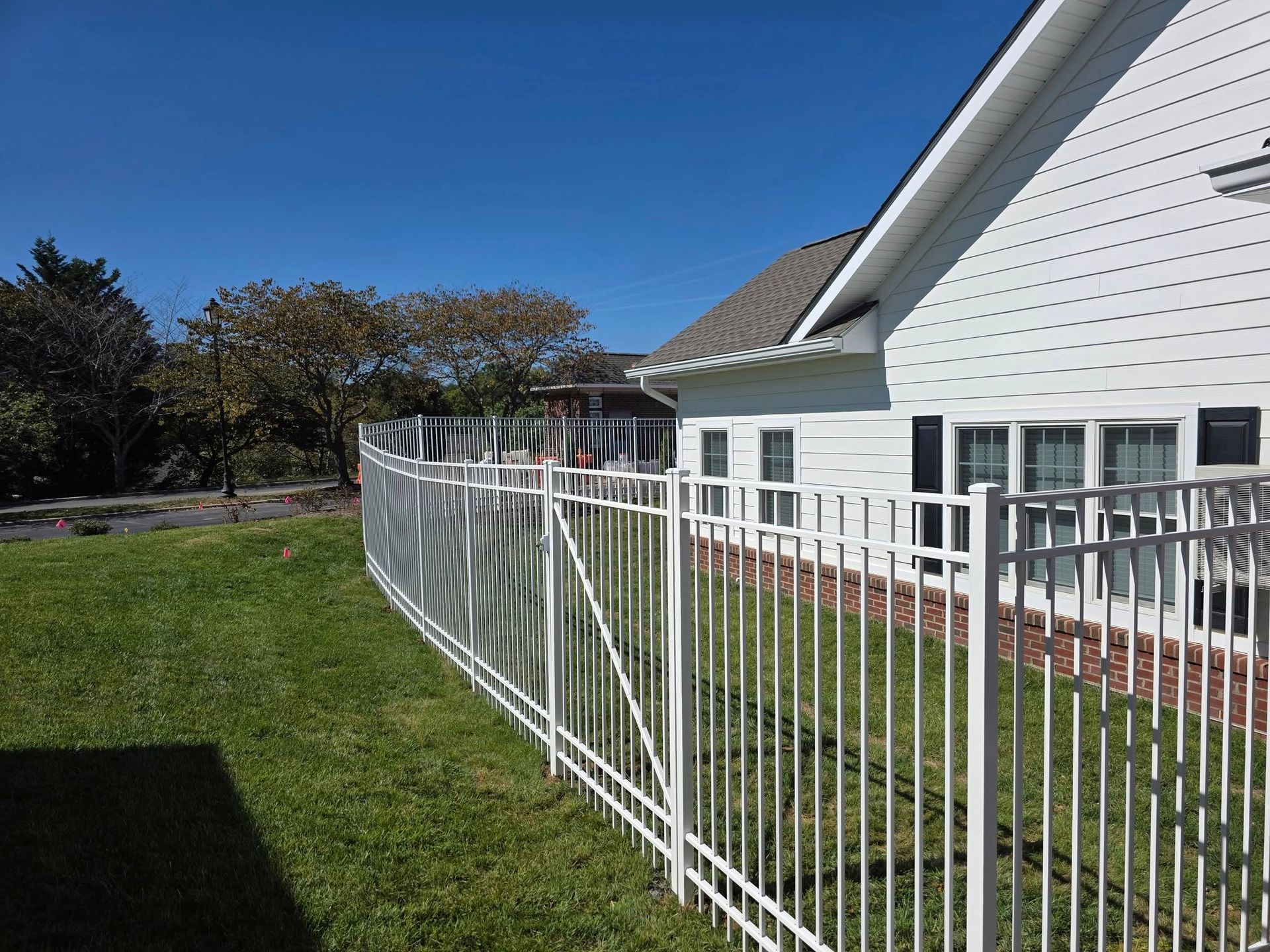 White metal fence along a white house with a green lawn and clear blue sky.