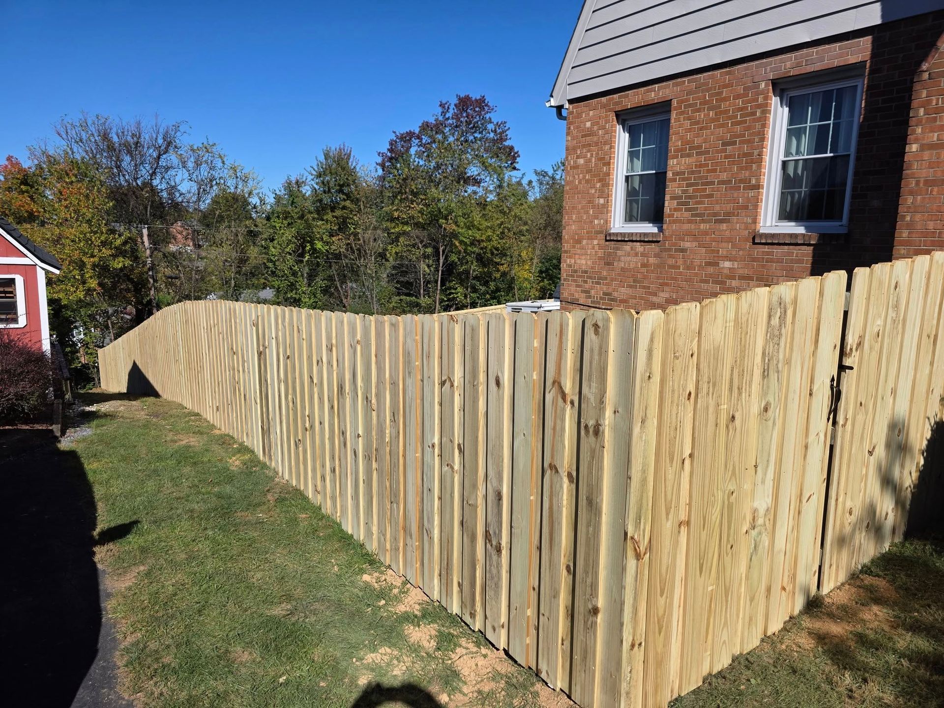 Wooden fence bordering a grassy yard next to a brick building.