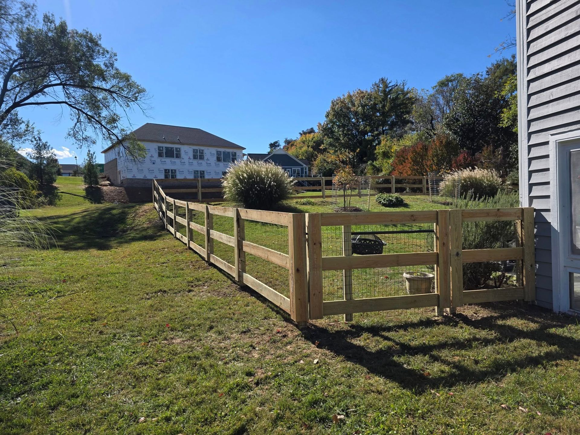 Wooden fence with a gate in a grassy yard, house in the background on a sunny day.