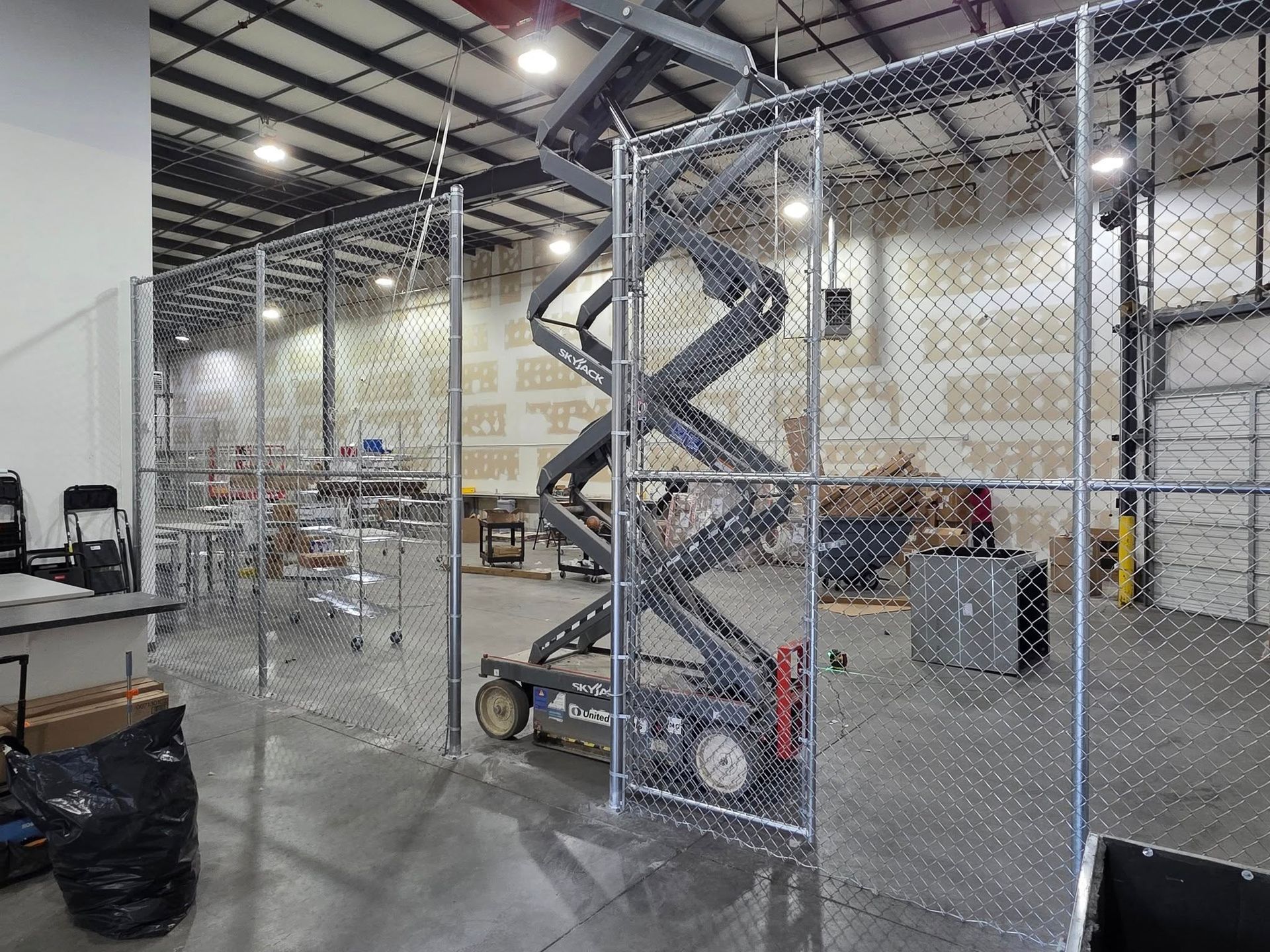 Chain-link fence encloses a scissor lift in a warehouse.