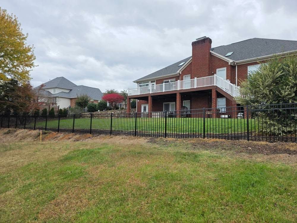 Black fence in front of a brick house with a white deck, under a cloudy sky.