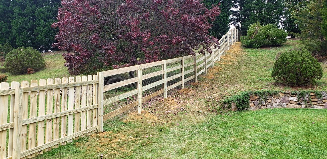 Wooden fence on a grassy hill, with bushes and trees in the background.