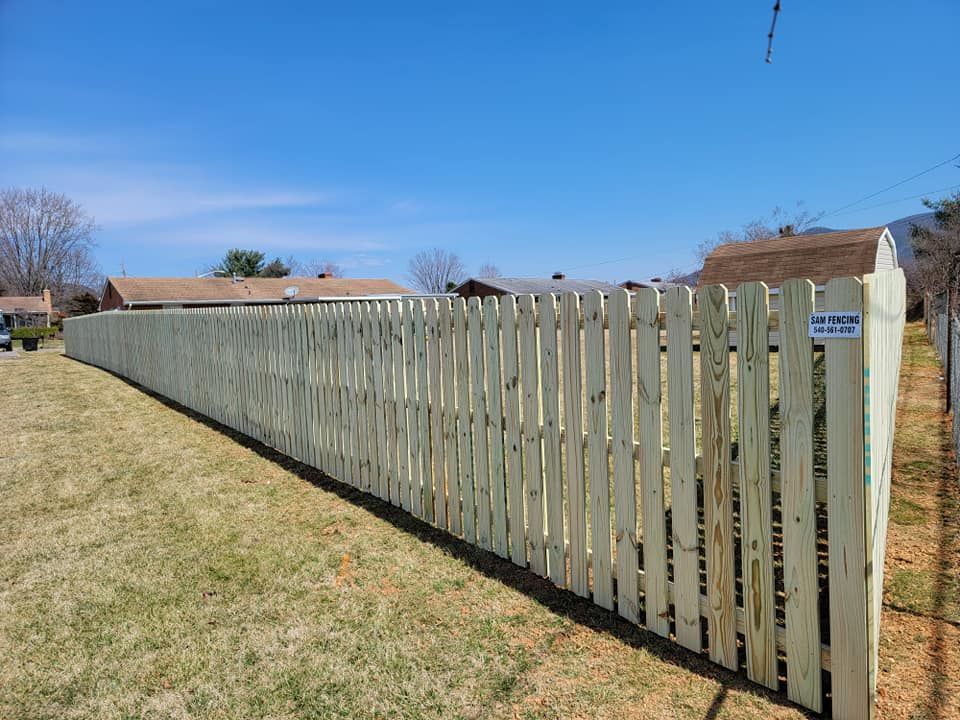 Wooden fence along a grassy yard, under a blue sky, with houses in the background.