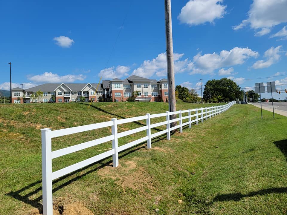 White fence along a grassy slope, with apartment buildings and a blue sky in the background.