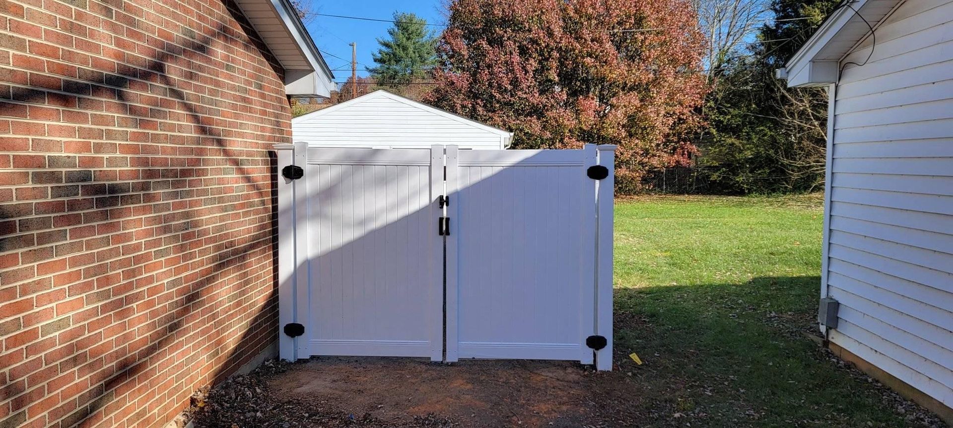 White double-door gate between a brick building and a white-sided building with grass in the background.