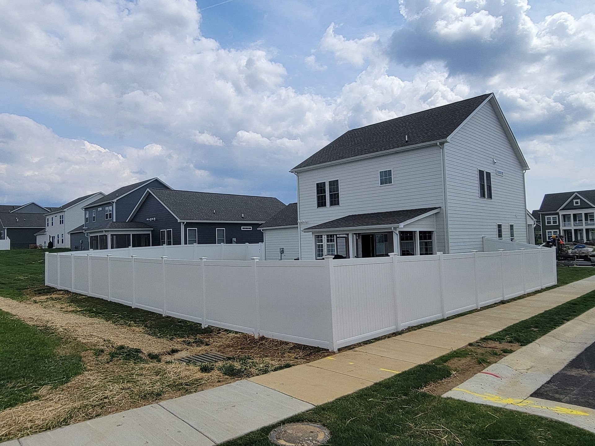 White vinyl fence surrounding a two-story house with a gray roof; blue sky with clouds.